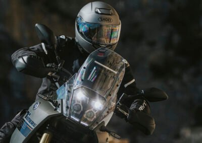 A rider wearing the Shoei Neotec 3 while riding a touring motorcycle on a winding road.