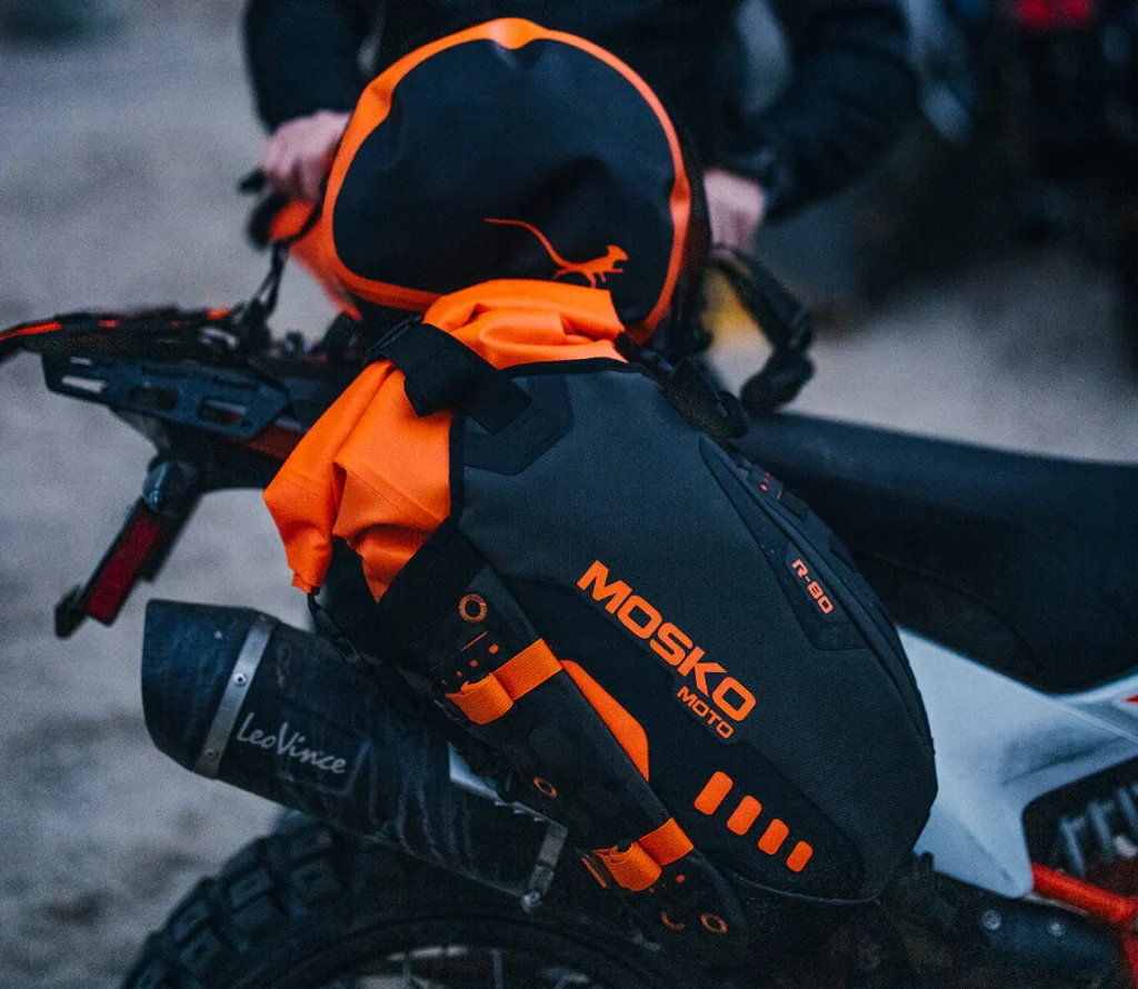 The complete Mosko Moto Reckless 80L (V4.0) system mounted on a KTM 890 Adventure R in a rugged, rocky environment.