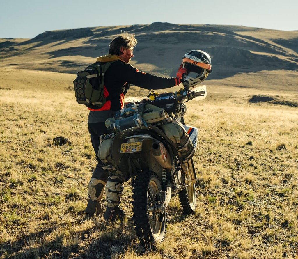 The Mosko Moto Reckless 80L's rear beavertail flap strapped down securely over a wet motorcycle rain jacket.