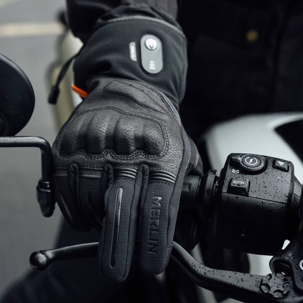A rider's hands wearing the Merlin Curborough gloves, gripping the handlebars of a modern classic motorcycle.